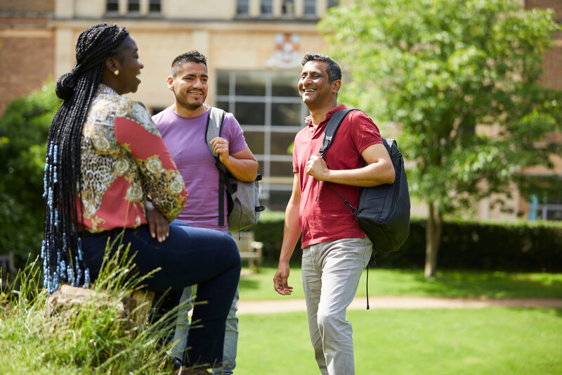 Masters students holding books chat together